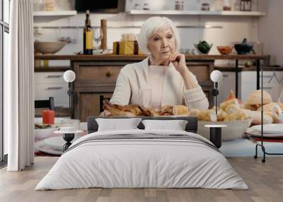 lonely and thoughtful senior woman sitting near thanksgiving dinner served on table in kitchen. Wall mural