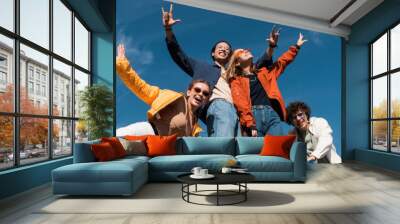 low angle view of cheerful multiethnic friends posing against blue cloudy sky, banner. Wall mural