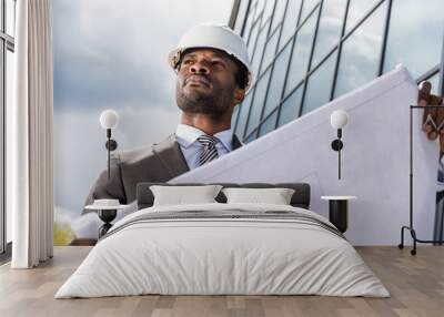 Low angle view of professional architect in hard hat holding blueprint outside modern building Wall mural