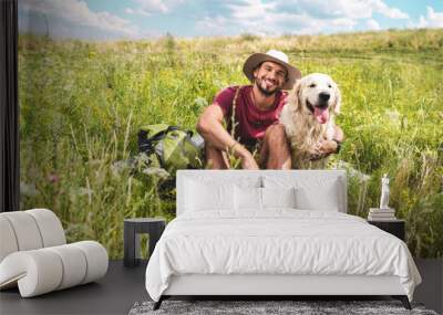 male traveler sitting with dog on green summer meadow Wall mural