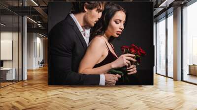 man with closed eyes embracing elegant woman with red roses in darkness Wall mural