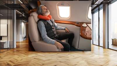 Mature businessman in neck pillow sleeping near laptop and coffee in private jet Wall mural