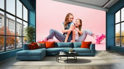 mother and daughter in denim clothes sitting on floor in roller skates and giving high five on pink Wall mural