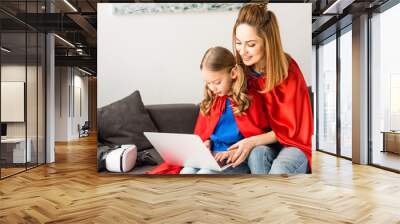 mother and daughter in red cloaks sitting on sofa and typing on laptop Wall mural