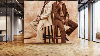 Multicultural men in elegant attire sitting on wooden stool. Wall mural