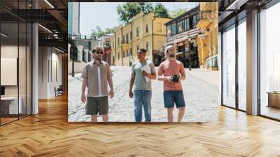 multiethnic tourists with map and vintage camera walking with tour guide on pavement of Andrews descent in Kyiv. Wall mural