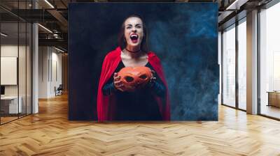 mystic woman in vampire costume holding jack o lantern on dark background with smoke Wall mural