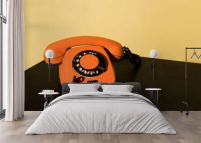 Old orange telephone standing on black surface on yellow background Wall mural