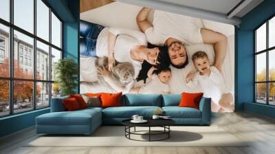 overhead view of smiling parents with two sons and grey british shorthair cat lying on bed together at home Wall mural