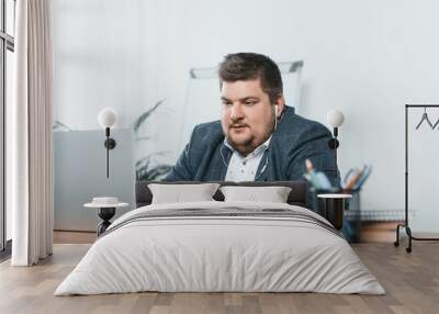 overweight businessman listening music with earphones while working on laptop in office Wall mural