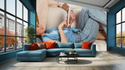 Panoramic crop of smiling girl using digital tablet while lying near man on couch at home Wall mural