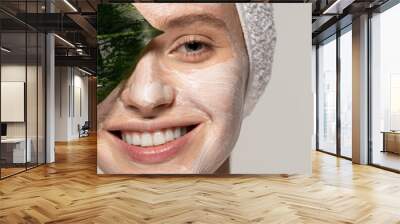 panoramic shot of attractive smiling girl with cosmetic mask on face posing with green leaf, isolated on grey Wall mural