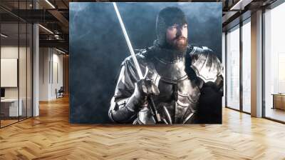 panoramic shot of handsome knight in armor looking away and holding sword on black background Wall mural