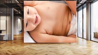 Panoramic shot of little barefoot child in diaper laying on bed with white bedding and smiling Wall mural