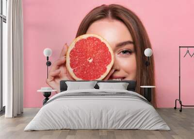 panoramic shot of smiling attractive girl holding cut grapefruit isolated on pink Wall mural