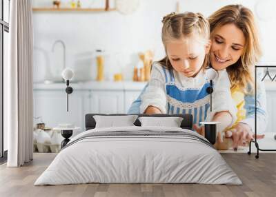 panoramic shot of smiling mother and cute daughter rolling dough on table Wall mural