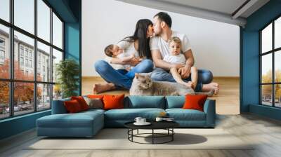 parents kissing each other with two sons and grey british shorthair cat on hands at home Wall mural