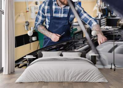 partial of tattooed technician examining car engine compartment on blurred foreground Wall mural