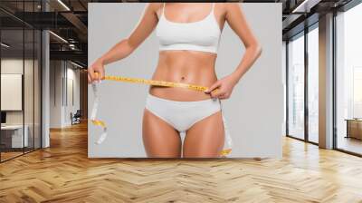 partial view of beautiful slim woman in underwear holding measuring tape on waist isolated on grey Wall mural