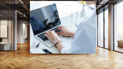 partial view of female doctor typing on laptop with blank screen at table in office Wall mural