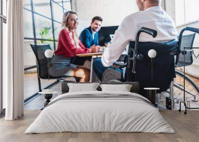 partial view of smiling businesspeople looking at colleague in wheelchair in office Wall mural