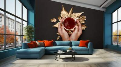 partial view of woman holding tea in mug near golden foliage on black background Wall mural