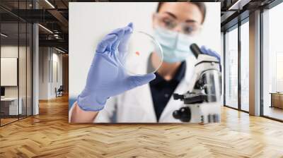 Petri dish in hand of blurred scientist near microscope in laboratory. Wall mural