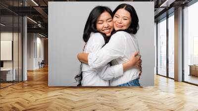 pleased asian mother and daughter in white shirts hugging isolated on grey Wall mural