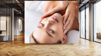 pleased young woman with closed eyes touching face and lying on massage table in spa salon Wall mural