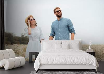 portrait of happy lovers in sunglasses holding hands in field with wild flowers Wall mural