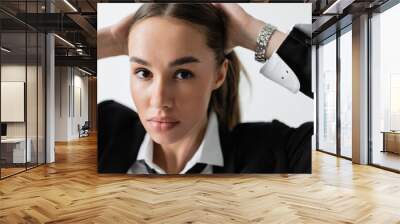 portrait of pretty woman in black suit with tie looking at camera while adjusting hair isolated on white. Wall mural