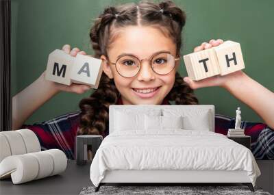 portrait of schoolchild holding wooden cubes with word math near blackboard Wall mural