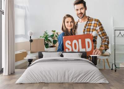 portrait of smiling couple holding sold red card at home with cardboard boxes Wall mural