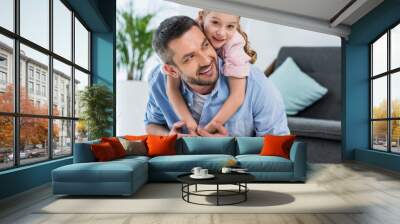 portrait of smiling father and little daughter piggybacking together at home Wall mural