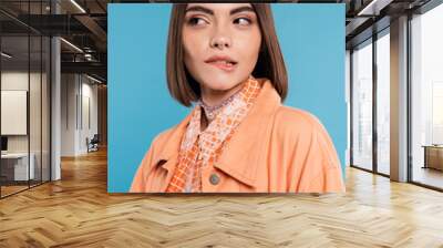 portrait of woman biting her lip, looking away on blue background, pensive, flirty, orange shirt, ge Wall mural