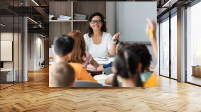 positive african american teacher pointing at blurred girl raising hand in classroom Wall mural