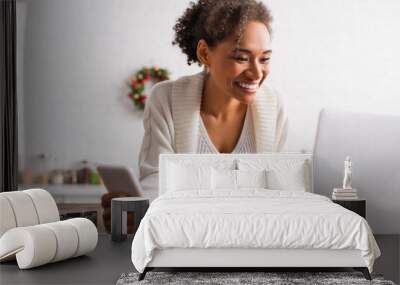 Positive african american woman with smartphone using laptop near cookie cutters in kitchen Wall mural