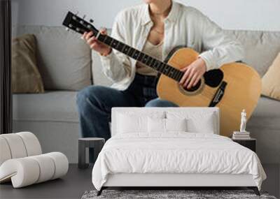 positive and blonde woman playing acoustic guitar while sitting on couch. Wall mural