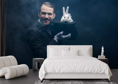 positive magician in suit showing trick with white rabbit in hat, dark room with smoke Wall mural