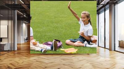 Positive multiethnic schoolkids holding sandwiches near backpacks on grass in park, banner. Wall mural