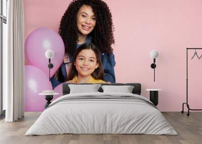 Positive woman looking at camera near daughter and party balloons isolated on pink. Wall mural