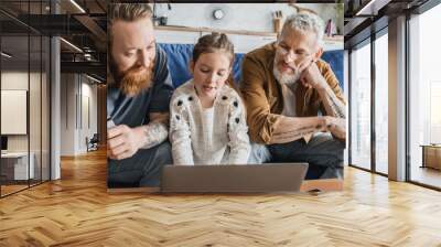 Preteen girl using laptop near tattooed same sex parents with credit card at home, banner.  Wall mural