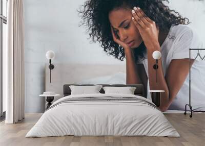 pretty african american woman holding hands near head while suffering from headache in bedroom Wall mural