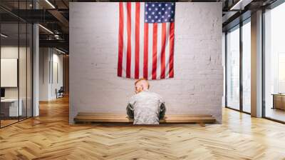 rear view of soldier in military uniform praying with american flag on white brick wall, americas independence day concept Wall mural