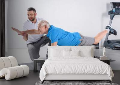 rehabilitation therapist helping smiling senior man exercising on mat Wall mural