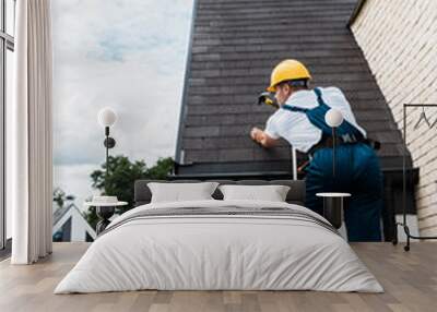 repairman in uniform and helmet repairing roof while standing on ladder Wall mural