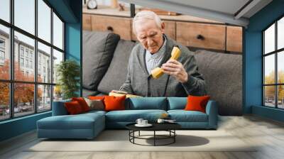 retired man looking at old phone while sitting on sofa Wall mural