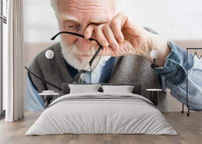 Sad senior man holding glasses, and covering eye of his hand Wall mural