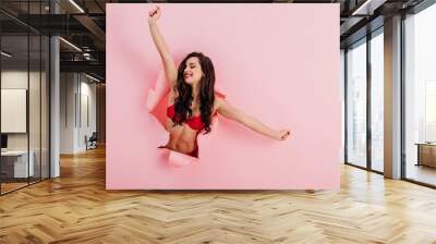 seductive, smiling girl in red lingerie stretching in paper hole on pink background Wall mural