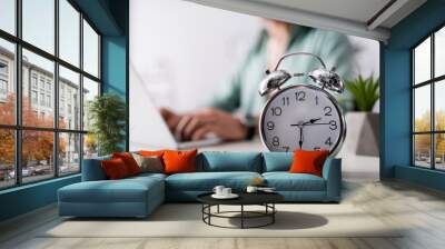 Selective focus of alarm clock on table near man using laptop at home, concept of time management Wall mural